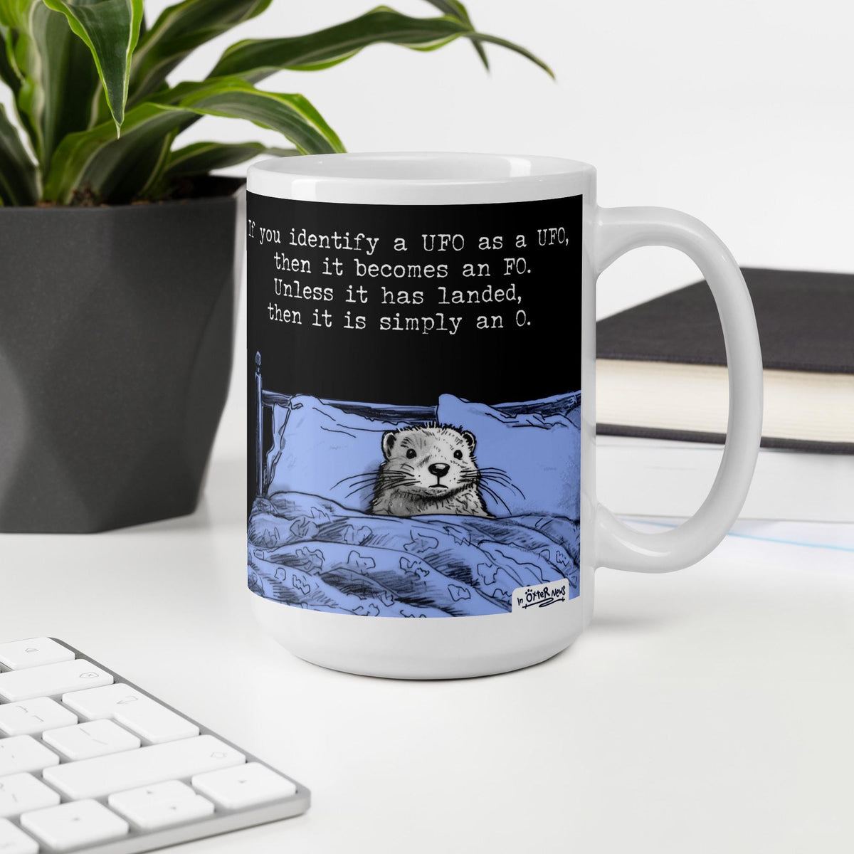 The UFO otter mug, 15 oz, on a desk with a plant and books